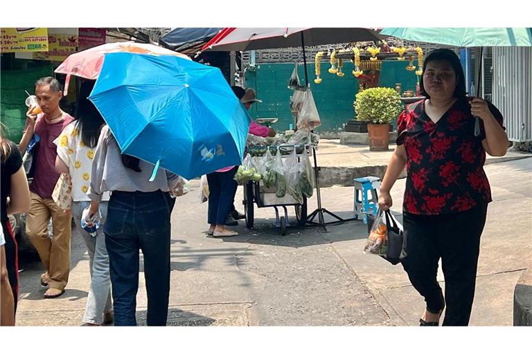 Menschen schützen sich in Bangkok mit Schirmen vor der extremen Hitze und vor der Sonne.