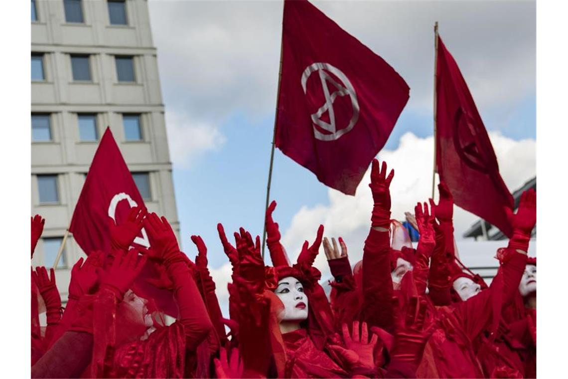 Aktivisten von Extinction Rebellion gehen in roten Gewändern und mit weiß angemalten Gesichtern über den Potsdamer Platz in Berlin. Foto: Paul Zinken/dpa