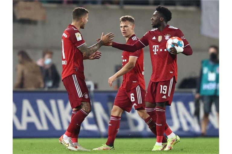 Alphonso Davies (r) klatscht nach dem Sieg mit Lucas Hernández (l) ab. Daneben steht Joshua Kimmich. Foto: Daniel Karmann/dpa