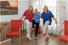 Als Ergo-Scouts motivieren Laura Kübler (links) und Anette Erb (rechts) nicht nur ihr Team, sondern auch die Bewohner, sich zwischendurch zu bewegen – so wie die 94-jährige Olga Demel, die beim Einbeinstand mitmacht. Foto: Stefan Bossow