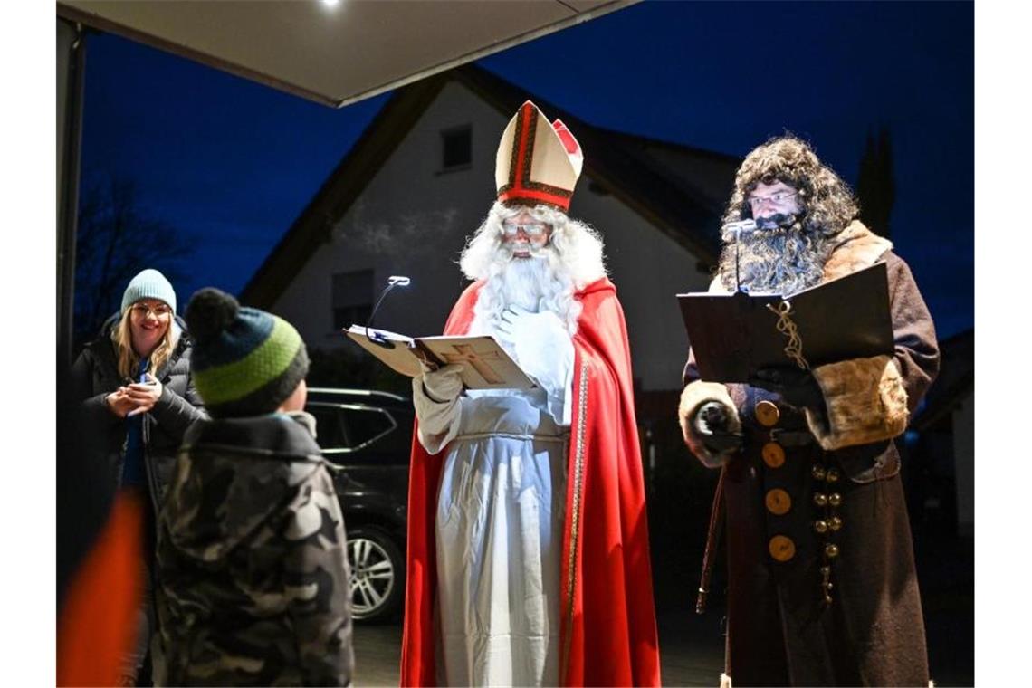 Als Nikolaus und sein Knecht Ruprecht verkleidet besuchen Erich Schwarz (in rot und mit Mitra) und Michael Huber (Ruprecht) eine Familie. Foto: Felix Kästle/dpa