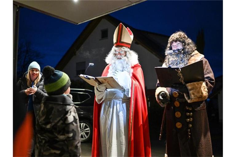 Als Nikolaus und sein Knecht Ruprecht verkleidet besuchen Erich Schwarz (in rot und mit Mitra) und Michael Huber (Ruprecht) eine Familie. Foto: Felix Kästle/dpa