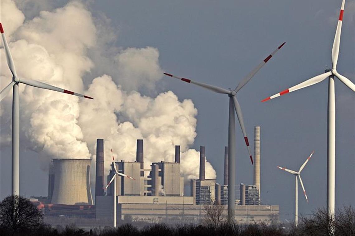 Alte und neue Technik: Rauch und Dampf steigen aus einem Braunkohlekraftwerk, im Vordergrund stehen Windräder. Foto: Oliver Berg/dpa