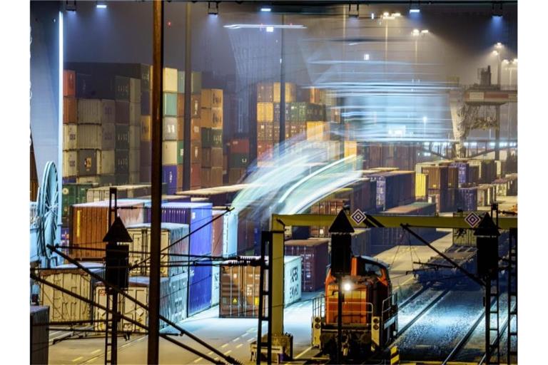 Am Containerbahnhof Frankfurt-Ost stehen am frühen Morgen hunderte Container, während im Vordergrund ein Kran einen weiteren von einem angekommenen Güterzug hinzufügt. Foto: Frank Rumpenhorst/dpa