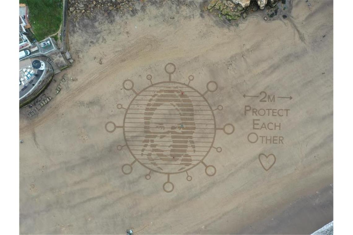 Am Strand in der Stadt Whitby wurde in den Sand ein riesiges Kunstwerk gemalt, das auf den Mindestabstand von zwei Metern während der Corona-Pandemie hinweist. Foto: Richard Mccarthy/PA Wire/dpa