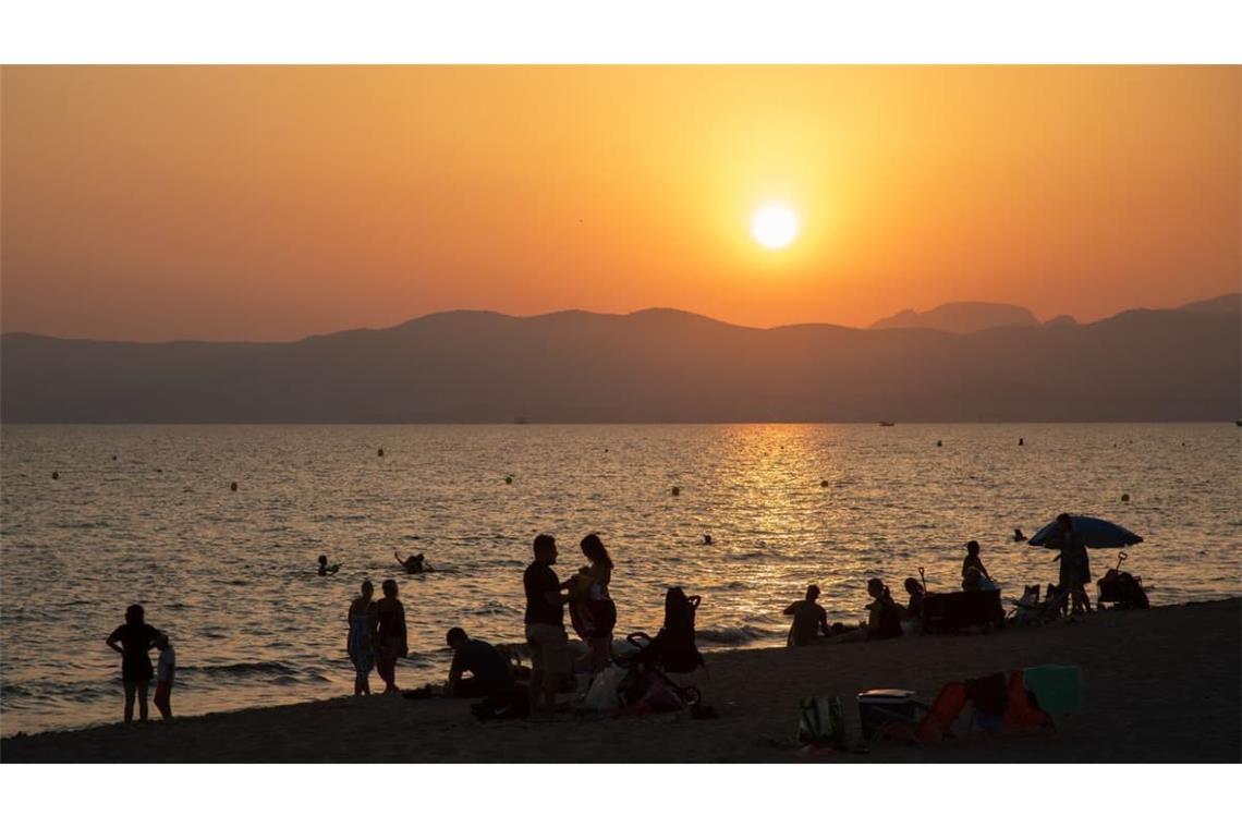 Am Strand von Playa de Palma auf Mallorca baden Menschen bei Sonnenuntergang im Meer. Die hohen Temperaturen locken viele Einheimische und Besucher an, sich bei Sonnenuntergang und in der Nacht am Meer zu erfrischen.