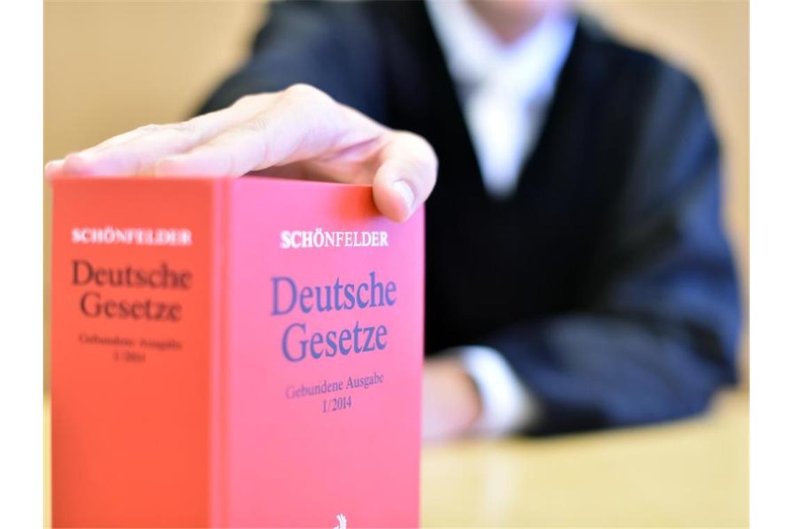 An der Richterbank eines Sitzungssaals sitzt ein Richter hinter einem Buch mit Deutschen Gesetzen. Foto: Uli Deck/dpa/Symbolbild