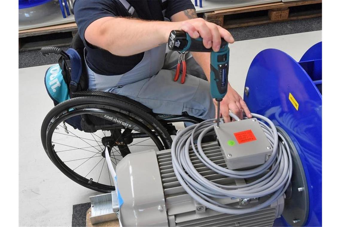 An einem Arbeitsplatz für Motorklemmen ist ein Mitarbeiter im Rollstuhl mit Montagearbeiten beschäftigt. Foto: Hendrik Schmidt/zb/dpa