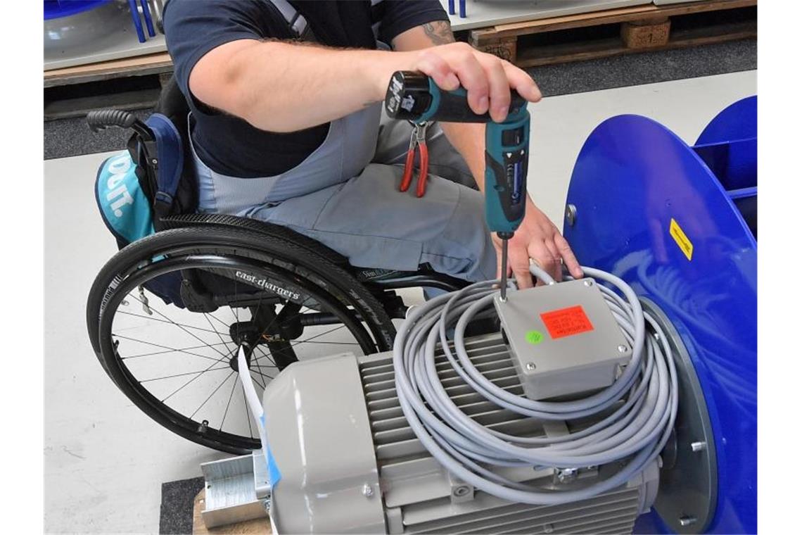 An einem Arbeitsplatz für Motorklemmen ist ein Mitarbeiter im Rollstuhl mit Montagearbeiten beschäftigt. Foto: Hendrik Schmidt/zb/dpa