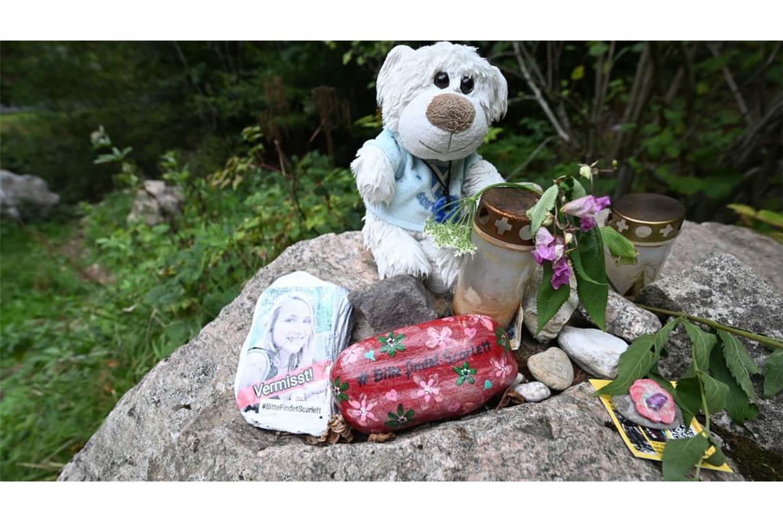 An einem Stein an einem Wanderparkplatz am Schluchtensteig liegen Blumen, ein Kuscheltier, ein bemalter Stein mit der Aufschrift "Vermisst" und einem Foto.