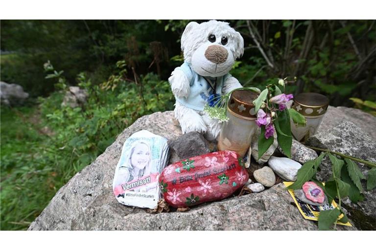 An einem Stein an einem Wanderparkplatz am Schluchtensteig liegen Blumen, ein Kuscheltier, ein bemalter Stein mit der Aufschrift "Vermisst" und einem Foto.