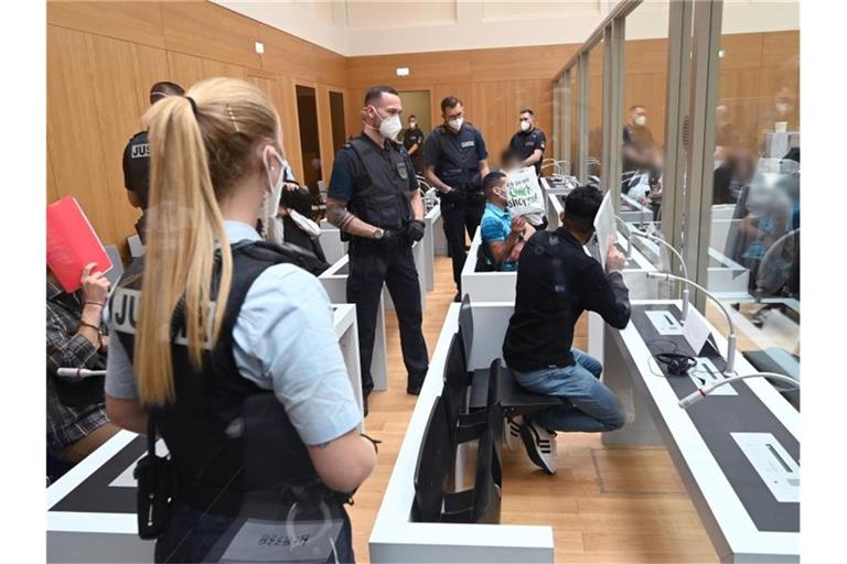 Angeklagte schützen vor Prozessbeginn ihre Gesichter mit Aktenordnern vor Kameras. Foto: Bernd Weißbrod/dpa