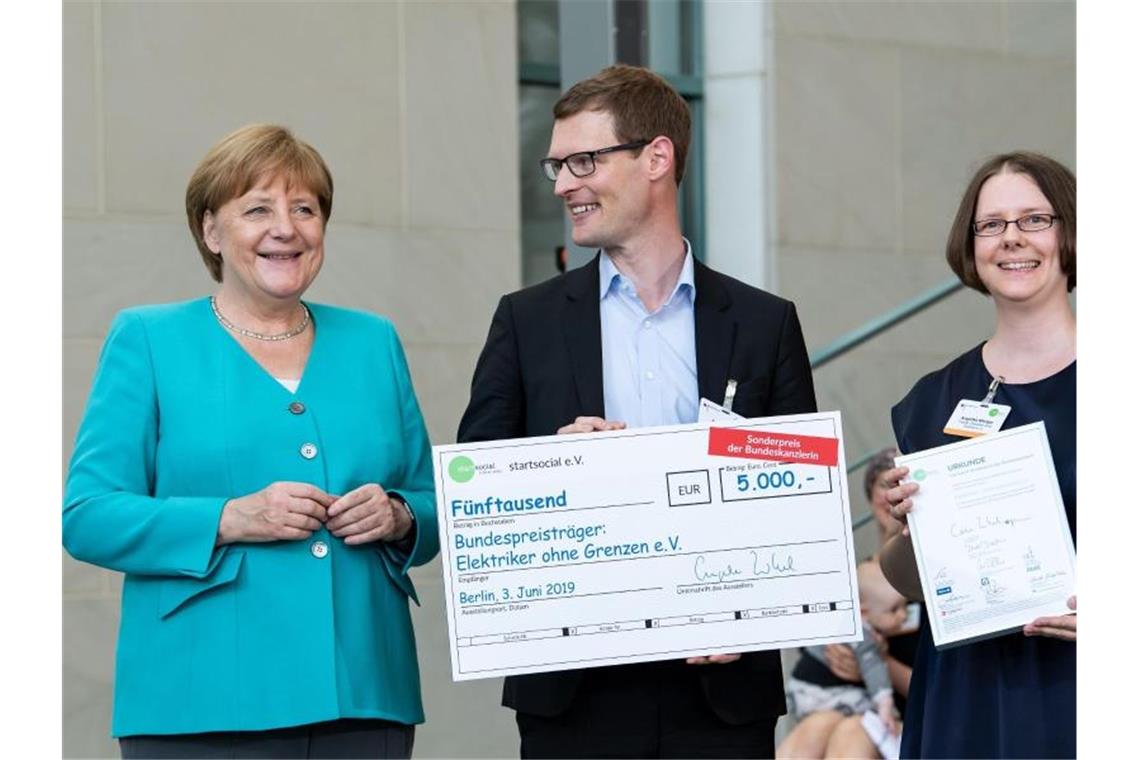 Angela Merkel (l, CDU) zeichnet Sylvain Volpp (M) und Angelika Wenger vom Projekt „Elektriker ohne Grenzen“ aus. Foto: Bernd von Jutrczenka
