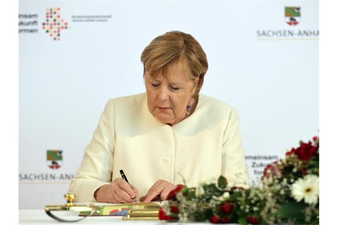 Angela Merkel trägt sich vor Beginn des Festakts in das Goldene Buch der Stadt Halle ein. Foto: Jan Woitas/dpa POOL/dpa