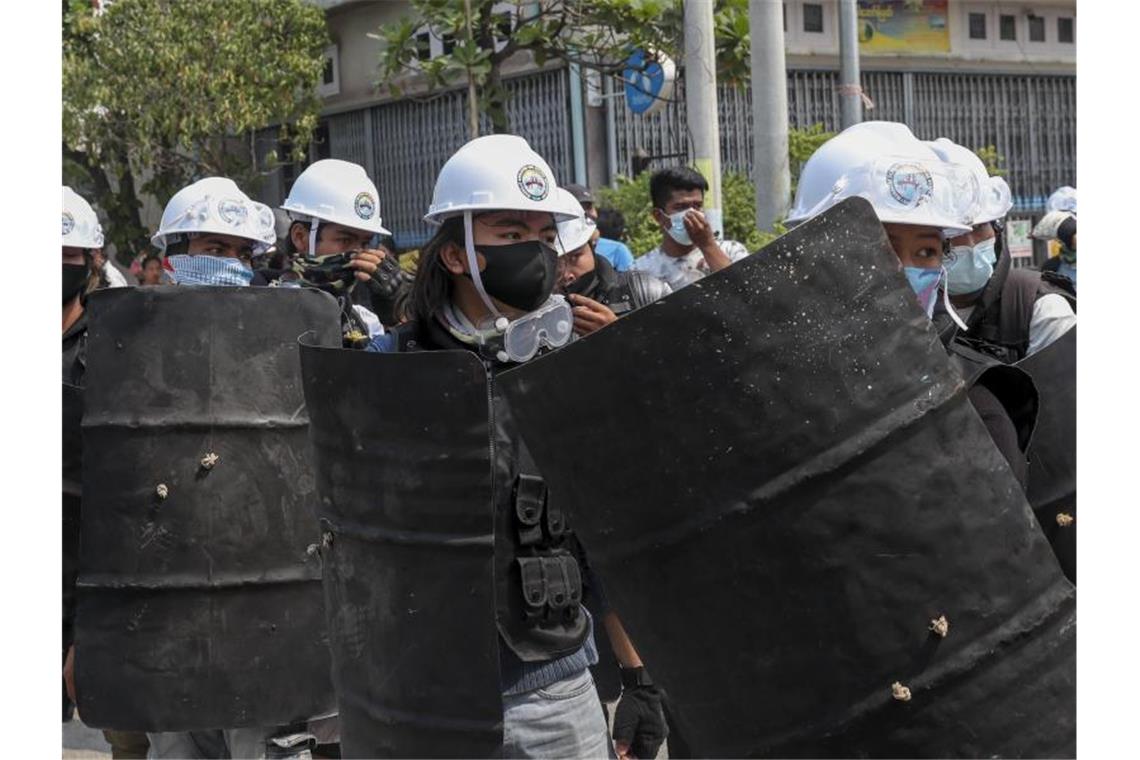 Militär umzingelt Demonstranten in Myanmar Anti-Putsch-Demonstranten gehen mit behelfsmäßigen Schilden, als ein Konvoi von Soldaten und Polizisten ankommt. Foto: Str/AP/dpa