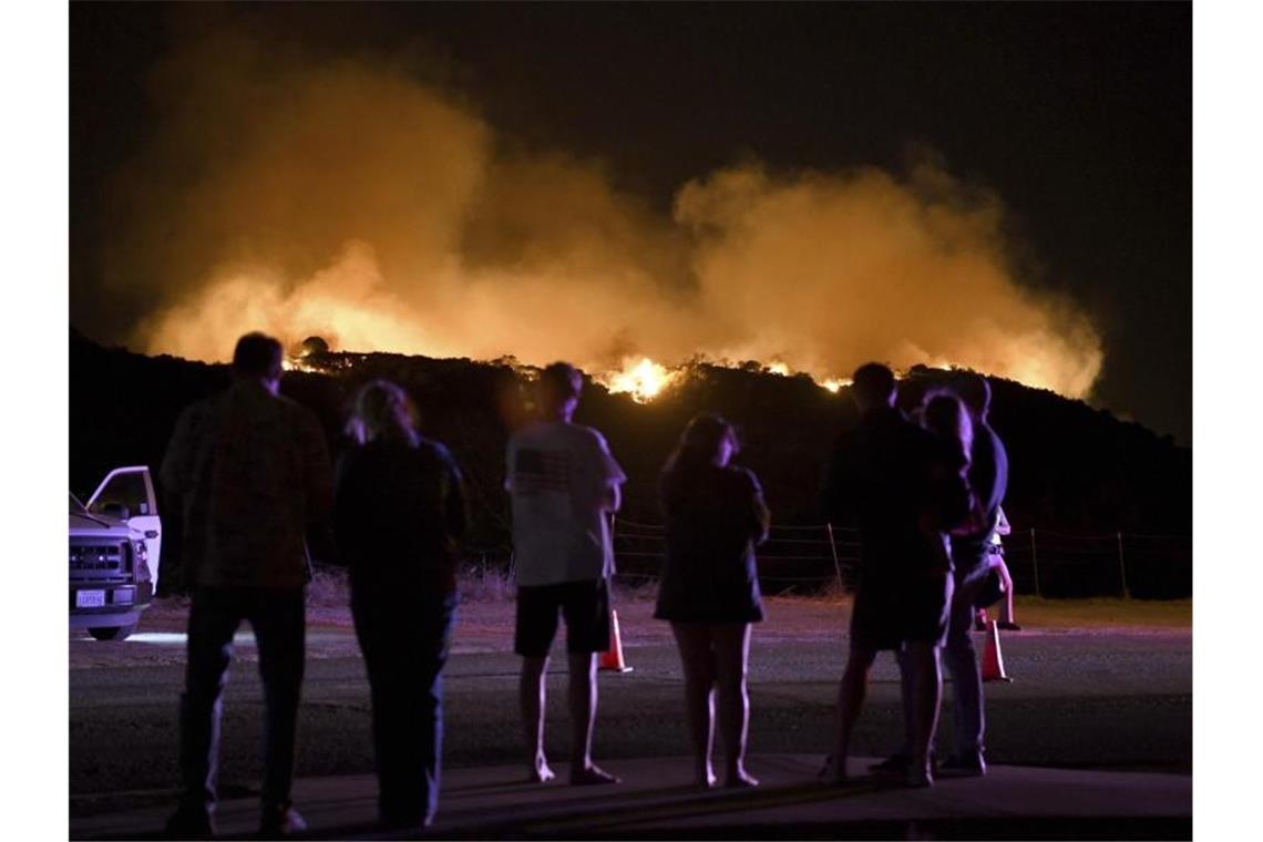 Anwohner beobachten einen Waldbrand unweit der Straße. Foto: Michael Owen Baker/AP/dpa