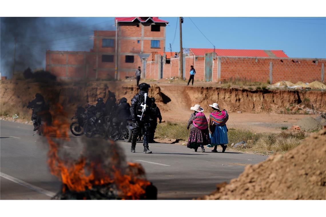 Anwohner gehen an einem Polizisten vorbei, der in Bolivien an einer brennenden Barrikade steht.