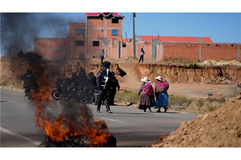 Anwohner gehen an einem Polizisten vorbei, der in Bolivien an einer brennenden Barrikade steht.
