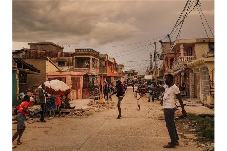 Anwohner stehen bei Sonnenuntergang auf einer Straße in Les Cayes, Haiti. Foto: Matias Delacroix/AP/dpa