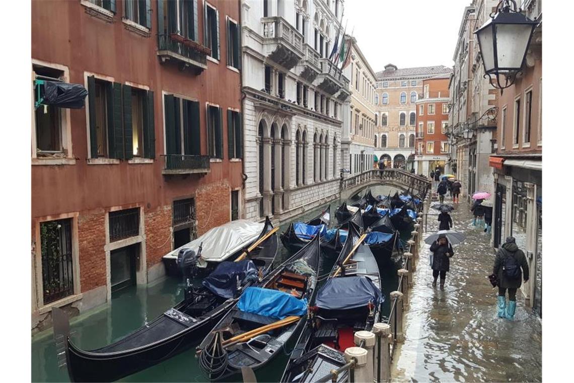 Anwohner waten durch eine überflutete Straße. Foto: -/ComunicareVenezia/dpa