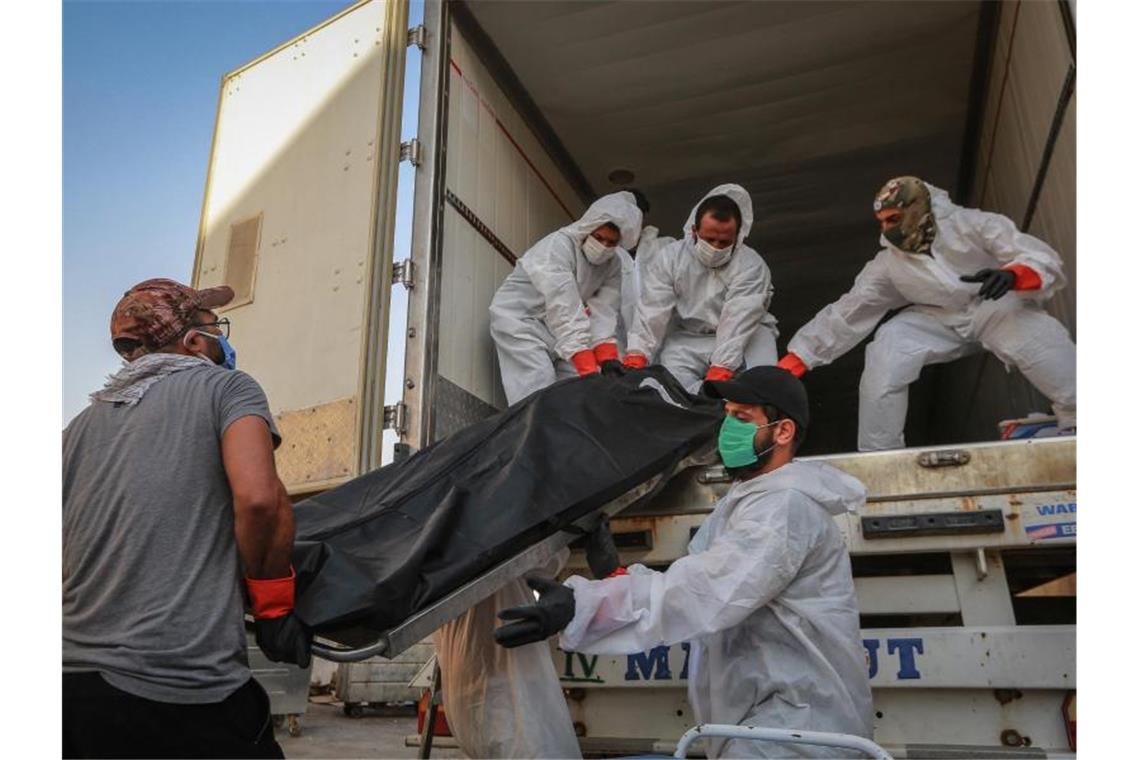 Arbeiter in Schutzkleidung beladen in Bagdad einen Kühlwagen mit Leichen von Menschen, die am Coronavirus gestorben sind. Foto: Ameer Al Mohammedaw/dpa