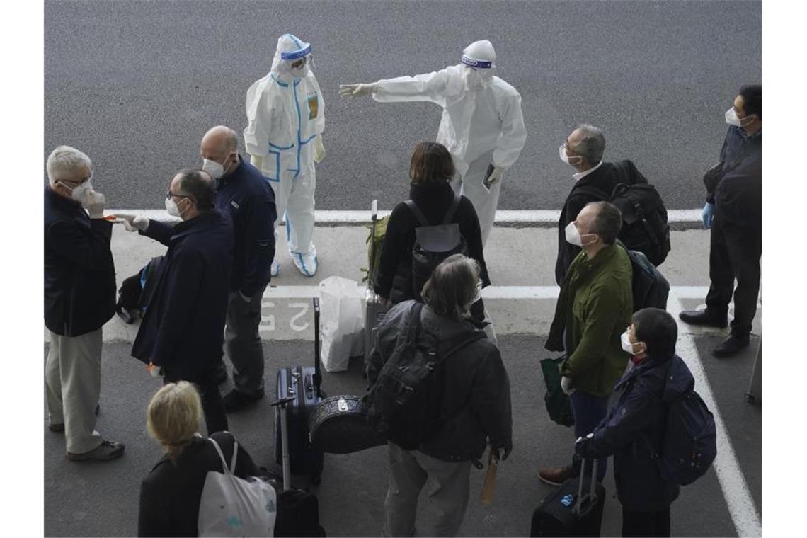 Arbeiter in Schutzkleidung sprechen mit Mitgliedern eines Teams der Weltgesundheitsorganisation (WHO) am Flughafen in Wuhan. Das globale Forscherteam soll eine Untersuchung über den Ursprung des Coronavirus durchführen. Foto: Ng Han Guan/AP/dpa