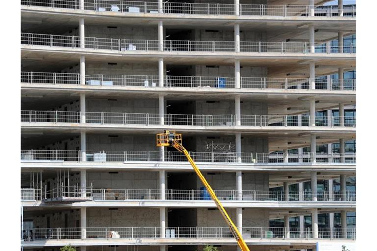 Arbeiter montieren von einer Hebebühne aus Teile an einem Neubau. Foto: Jens Büttner/zb/dpa/Symbolbild