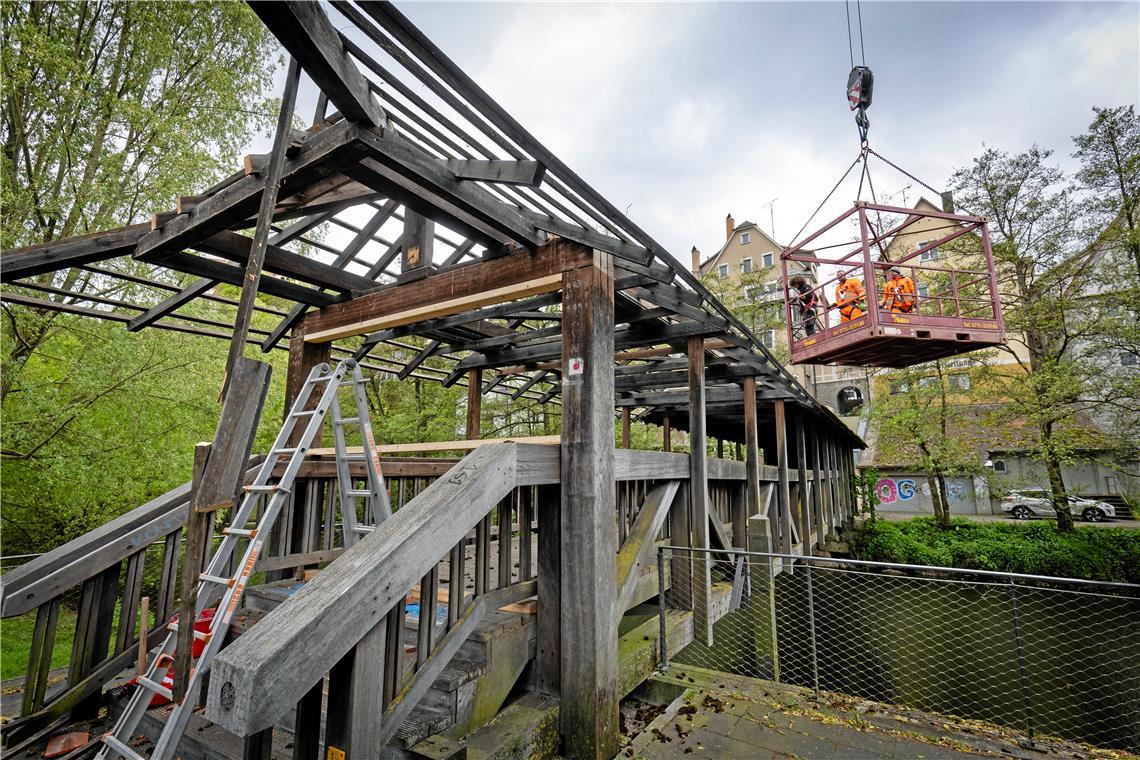 Abschied vom Backnanger Holzsteg über die Murr Arbeitsplatz am Haken: Um die Dachziegel entfernen zu können, wird der Bautrupp von einem Autokran an die richtige Stelle gehievt.