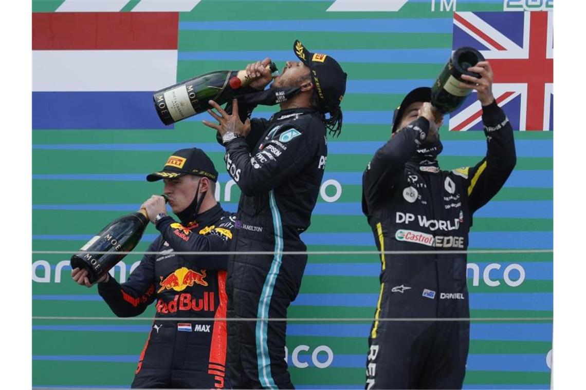 Auf dem Podest genehmigen sich der Zweitplatzierte Max Verstappen (l-r), Sieger Lewis Hamilton und Daniel Ricciardo zunächst einen großen Schluck. Foto: Ronald Wittek/Pool EPA/AP/dpa