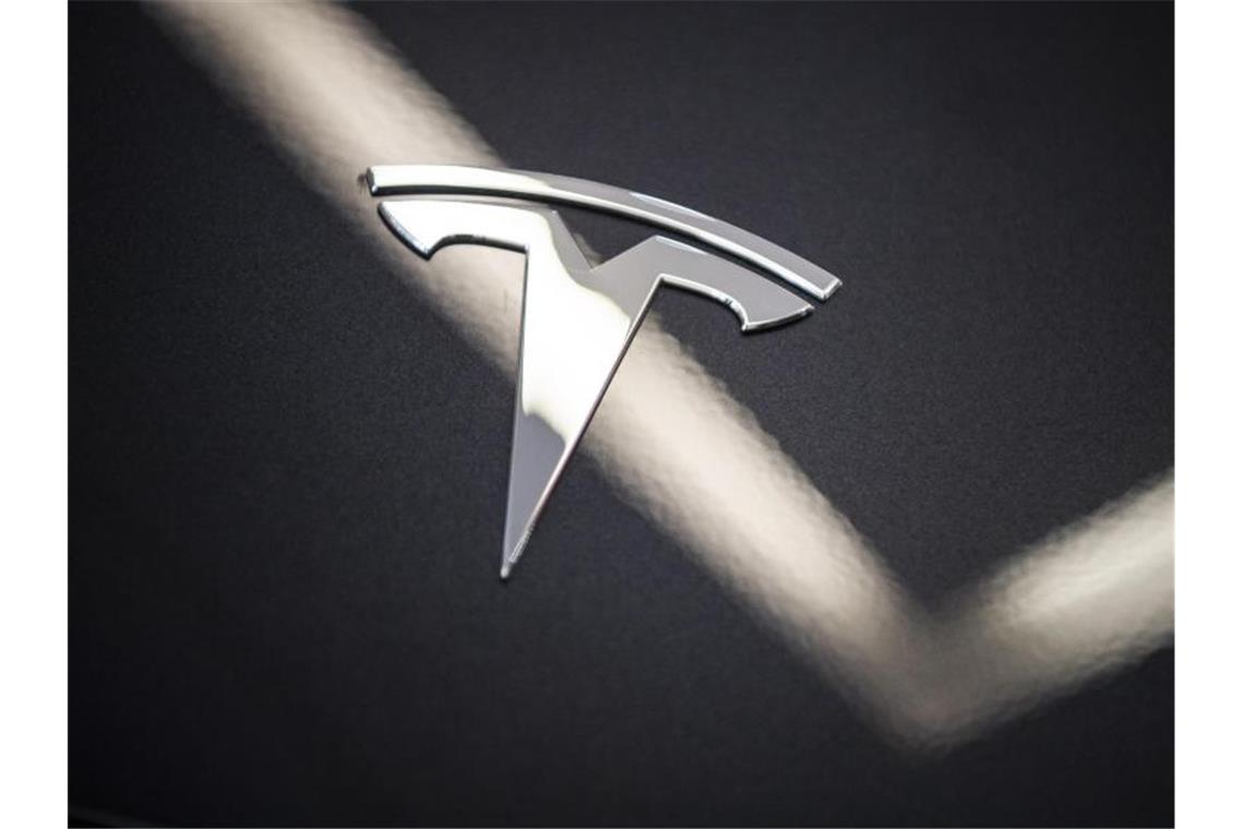 Auf der Motorhaube des Elektroautos Model 3 von Tesla in einem Ausstellungsraum ist das Logo zu sehen. Foto: Christophe Gateau/dpa