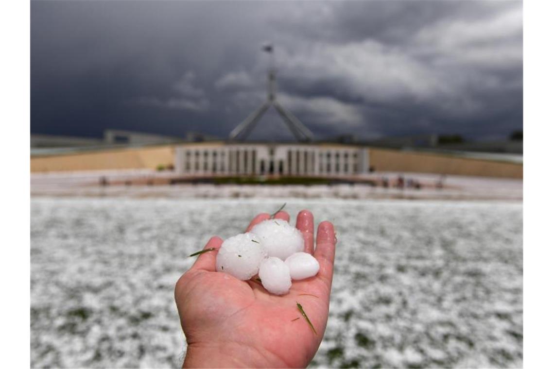 Auf einer Hand liegen Golfballgroße Hagelkörner, die bei einem schweren Hagelsturm vor dem Parlamentsgebäude niedergegangen sind. Foto: Mick Tsikas/AAP/dpa