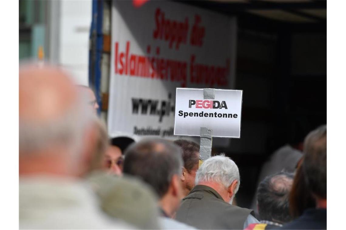 Auf einer Kundgebung von Pegida halten Anhänger ein Schild mit dem Schriftzug „Pegida Spendentonne“ in die Höhe. Foto: Zentralbild/dpa-Zentralbild/dpa