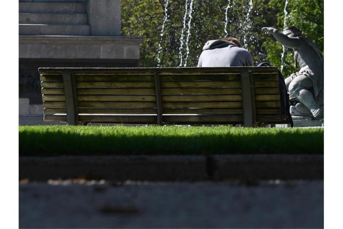 Auf einer Parkbank sitzt ein Mann, der auf sein Handy schaut. Foto: Bernd Weißbrod/dpa