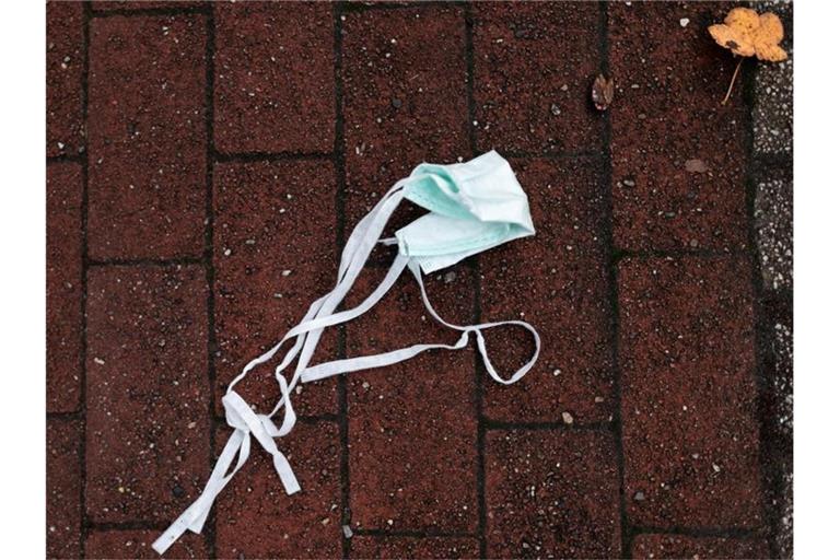 Auf einer Straße liegt ein Mund-Nasen-Schutz auf dem Boden. Foto: Fabian Strauch/dpa/Symbolbild