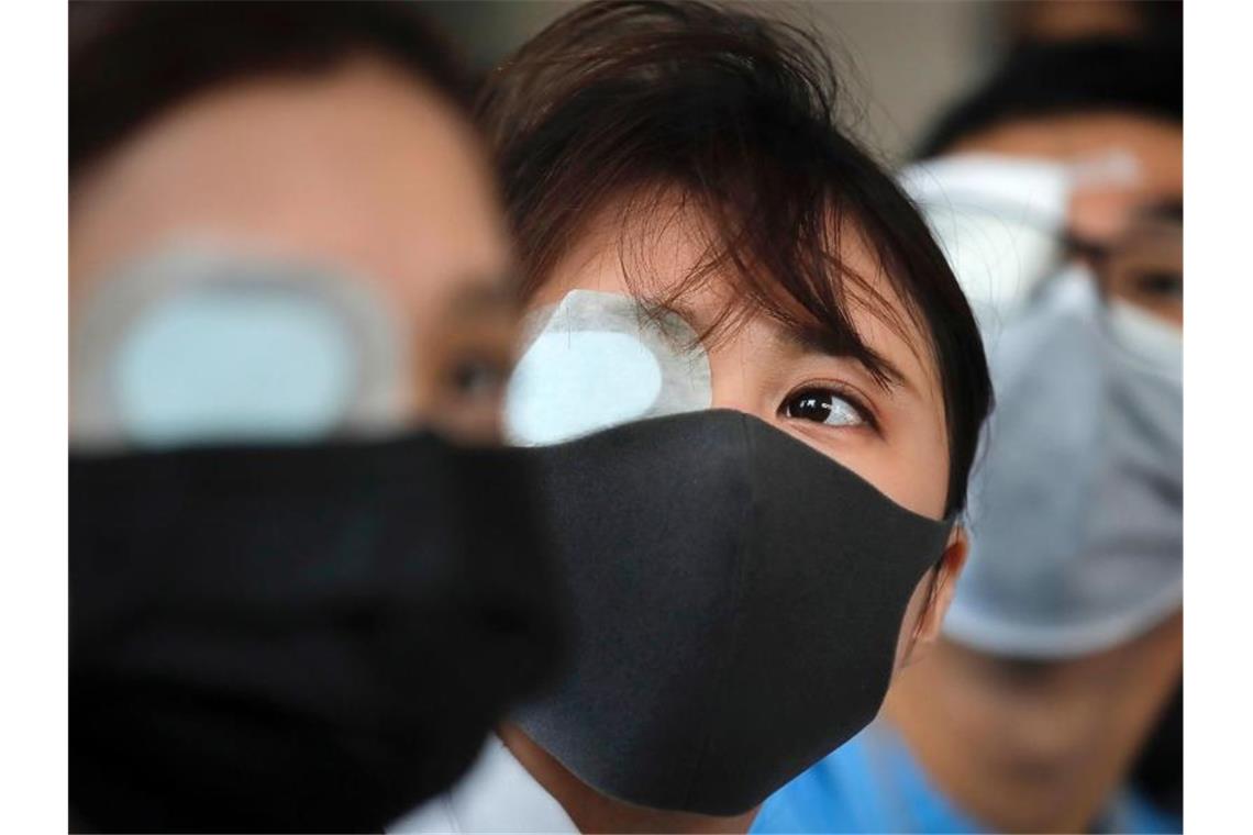 Heftige Zusammenstöße in Hongkongs Flughafen Augenklappe und Mundschutz sollen den Protest gegen die Polizei symbolisieren, die bei den Auseinandersetzungen im Flughafen eine Frau mit einem Gummigeschoss im Gesicht schwer verletzt haben soll. Foto: Kin Cheung/AP