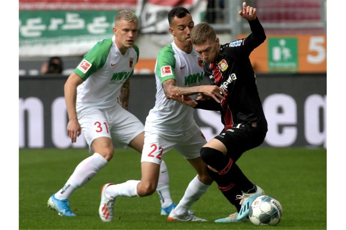 Augsburgs Iago (M) , Philipp Max (l) und Leverkusens Mitchell Weiser (r) kämpfen um den Ball. Foto: Stefan Puchner