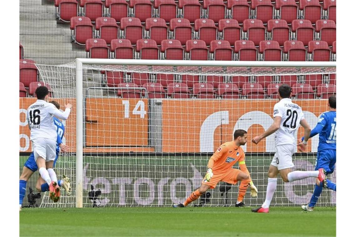 Augsburgs Mittelfeldspieler Ruben Vargas (l) erzielt den Treffer zum 1:0 - Hoffenheims Torwart Oliver Baumann (M) kann dem Ball nur hinterherschauen. Foto: Peter Kneffel/dpa
