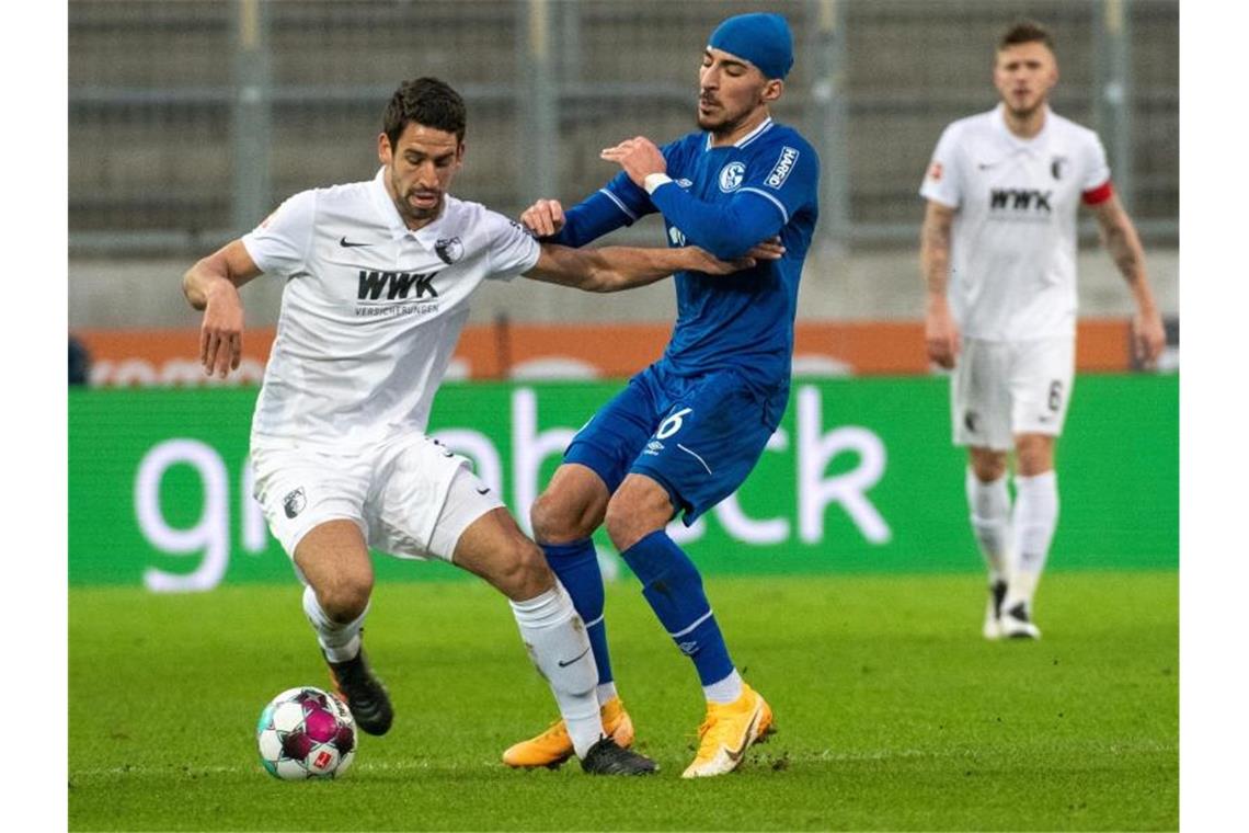 Augsburgs Rani Khedira (l) im Zweikampf mit Schalkes Nassim Boujellab. Foto: Stefan Puchner/dpa