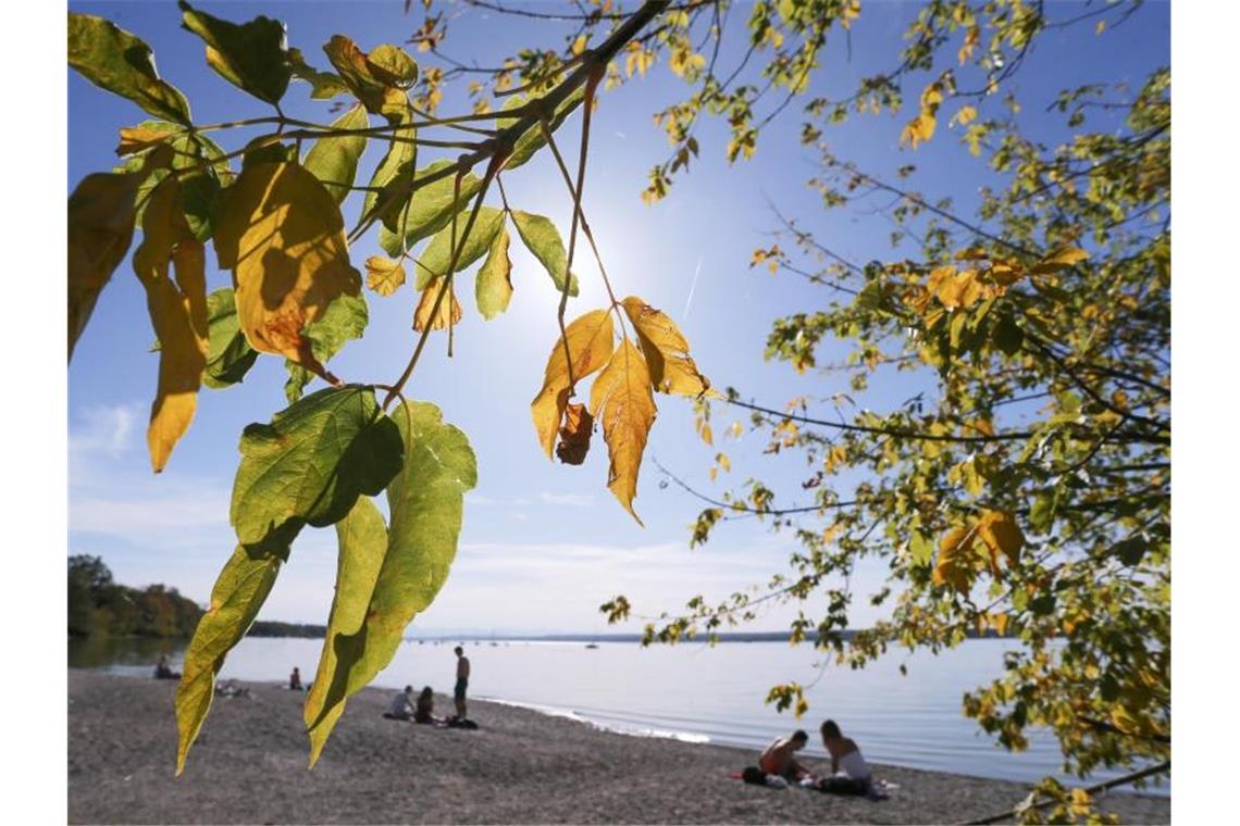 Ausflügler genießen am Ufer des Ammersees unter herbstlich gefärbten Bäumen den Sonnenschein. Foto: Karl-Josef Hildenbrand/dpa