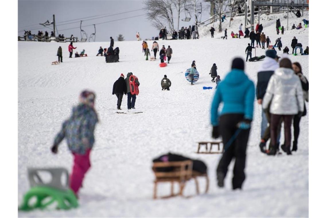 Ausflügler ziehen ihre Schlitten einen verschneiten Hang hoch. Die Stadt Winterberg bittet wegen der Corona-Pandemie auf Besuche in dem Wintersportort und an den Pisten im Sauerland zu verzichten. Foto: Marius Becker/dpa