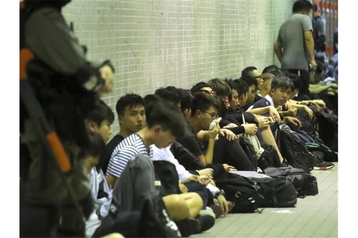 Ausgerüstete Polizisten stehen neben festgenommen Demonstranten. Foto: Kin Cheung/AP/dpa