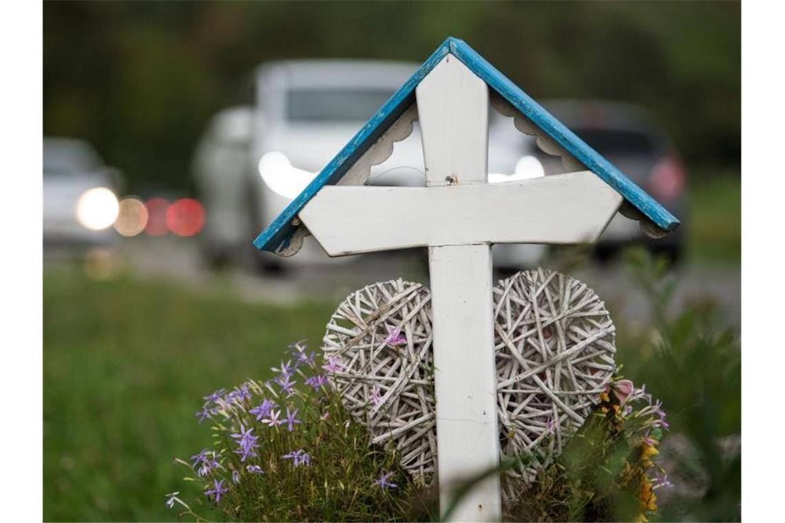 Autos fahren an einem weißen Kreuz für eine Unfalltote vorbei. Die Zahl der Todesopfer auf deutschen Straßen wird dieses Jahr voraussichtlich leicht steigen. Foto: Sebastian Gollnow