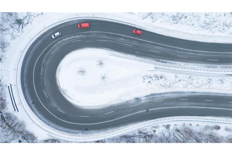 Autos fahren auf einer von Schnee geräumten Serpentine entlang. (Luftaufnahme mit einer Drohne).