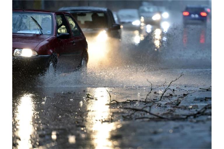 Autos fahren langsam durch eine tiefe Pfütze die sich durch Starkregen auf einer Straße gebildet hat. Foto: Caroline Seidel/dpa/Archivbild