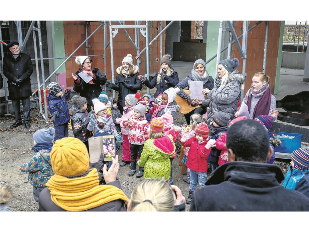 Richtfest am Kindergarten Sachsenweiler BACKNANG (inf). „In meinem Garten groß und schön, da soll nun bald mein Kindi stehn.“ So sangen die Kindergartenkinder gestern beim Richtfest am evangelischen Kindergarten Sachsenweiler. Der Neubau, der zurzeit nach den Plänen der Backnanger Architekten Sibylle und Tilman Nussbaum an der Stelle des abgebrochenen Kindergartens entsteht, kostet ungefähr 2,2 Millionen Euro und soll im Sommer nächsten Jahres fertig werden. Der Neubau bietet Platz, um eine dritte Gruppe zu eröffnen. Dekan Wilfried Braun und Pfarrerin Ulrike Heinrich verliehen dem Richtfest einen geistlichen Charakter. So hielt die Pfarrerin eine Andacht und begleitete den Richtspruch der Zimmerleute mit einem Gebet, und der Dekan stellte schon in der Begrüßung den kirchlichen Bezug her. Während der Bauzeit, die mit den Abbrucharbeiten im April begonnen hat, ist der Kindergarten mit seinen beiden Gruppen – den Bienen und den Schmetterlingen – in mehreren benachbarten Gebäuden untergekommen: in der Schule, bei der Mennonitengemeinde und in der evangelischen Kirche. Von dort aus verfolgen die Kinder, wie Kita-Leiterin Jutta Hofer erzählt, mit großem Interesse das Entstehen ihrer künftigen Bleibe und schauen auch öfter direkt dort vorbei. Foto: A. Becher