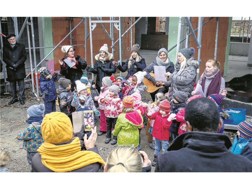 BACKNANG (inf). „In meinem Garten groß und schön, da soll nun bald mein Kindi stehn.“ So sangen die Kindergartenkinder gestern beim Richtfest am evangelischen Kindergarten Sachsenweiler. Der Neubau, der zurzeit nach den Plänen der Backnanger Architekten Sibylle und Tilman Nussbaum an der Stelle des abgebrochenen Kindergartens entsteht, kostet ungefähr 2,2 Millionen Euro und soll im Sommer nächsten Jahres fertig werden. Der Neubau bietet Platz, um eine dritte Gruppe zu eröffnen. Dekan Wilfried Braun und Pfarrerin Ulrike Heinrich verliehen dem Richtfest einen geistlichen Charakter. So hielt die Pfarrerin eine Andacht und begleitete den Richtspruch der Zimmerleute mit einem Gebet, und der Dekan stellte schon in der Begrüßung den kirchlichen Bezug her. Während der Bauzeit, die mit den Abbrucharbeiten im April begonnen hat, ist der Kindergarten mit seinen beiden Gruppen – den Bienen und den Schmetterlingen – in mehreren benachbarten Gebäuden untergekommen: in der Schule, bei der Mennonitengemeinde und in der evangelischen Kirche. Von dort aus verfolgen die Kinder, wie Kita-Leiterin Jutta Hofer erzählt, mit großem Interesse das Entstehen ihrer künftigen Bleibe und schauen auch öfter direkt dort vorbei. Foto: A. Becher