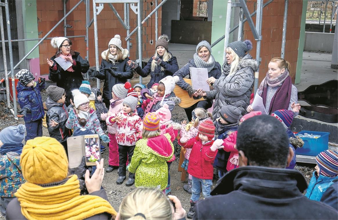 Richtfest am Kindergarten Sachsenweiler BACKNANG (inf). „In meinem Garten groß und schön, da soll nun bald mein Kindi stehn.“ So sangen die Kindergartenkinder gestern beim Richtfest am evangelischen Kindergarten Sachsenweiler. Der Neubau, der zurzeit nach den Plänen der Backnanger Architekten Sibylle und Tilman Nussbaum an der Stelle des abgebrochenen Kindergartens entsteht, kostet ungefähr 2,2 Millionen Euro und soll im Sommer nächsten Jahres fertig werden. Der Neubau bietet Platz, um eine dritte Gruppe zu eröffnen. Dekan Wilfried Braun und Pfarrerin Ulrike Heinrich verliehen dem Richtfest einen geistlichen Charakter. So hielt die Pfarrerin eine Andacht und begleitete den Richtspruch der Zimmerleute mit einem Gebet, und der Dekan stellte schon in der Begrüßung den kirchlichen Bezug her. Während der Bauzeit, die mit den Abbrucharbeiten im April begonnen hat, ist der Kindergarten mit seinen beiden Gruppen – den Bienen und den Schmetterlingen – in mehreren benachbarten Gebäuden untergekommen: in der Schule, bei der Mennonitengemeinde und in der evangelischen Kirche. Von dort aus verfolgen die Kinder, wie Kita-Leiterin Jutta Hofer erzählt, mit großem Interesse das Entstehen ihrer künftigen Bleibe und schauen auch öfter direkt dort vorbei. Foto: A. Becher