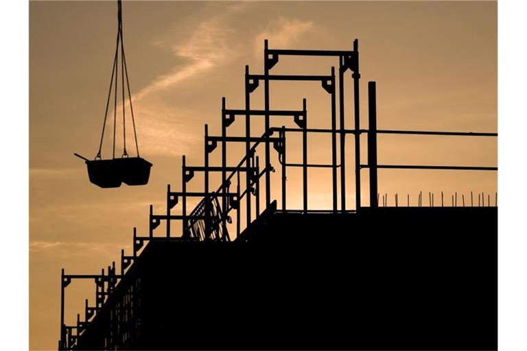 Bauarbeiter bauen bei Sonnenaufgang an einem Wohnhaus. Foto: Julian Stratenschulte/Archivbild