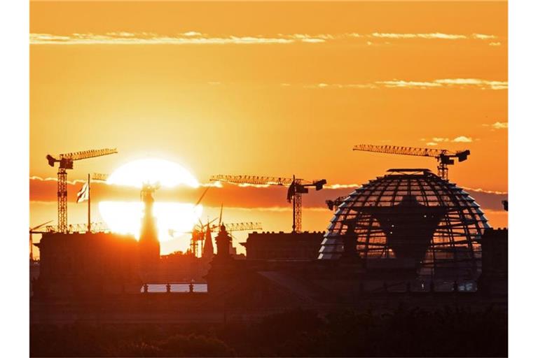 Baukräne und die Kuppel des Reichstagsgebäudes in Berlin. Die deutsche Wirtschaft kommt wieder in Schwung. Foto: Fabian Sommer/dpa