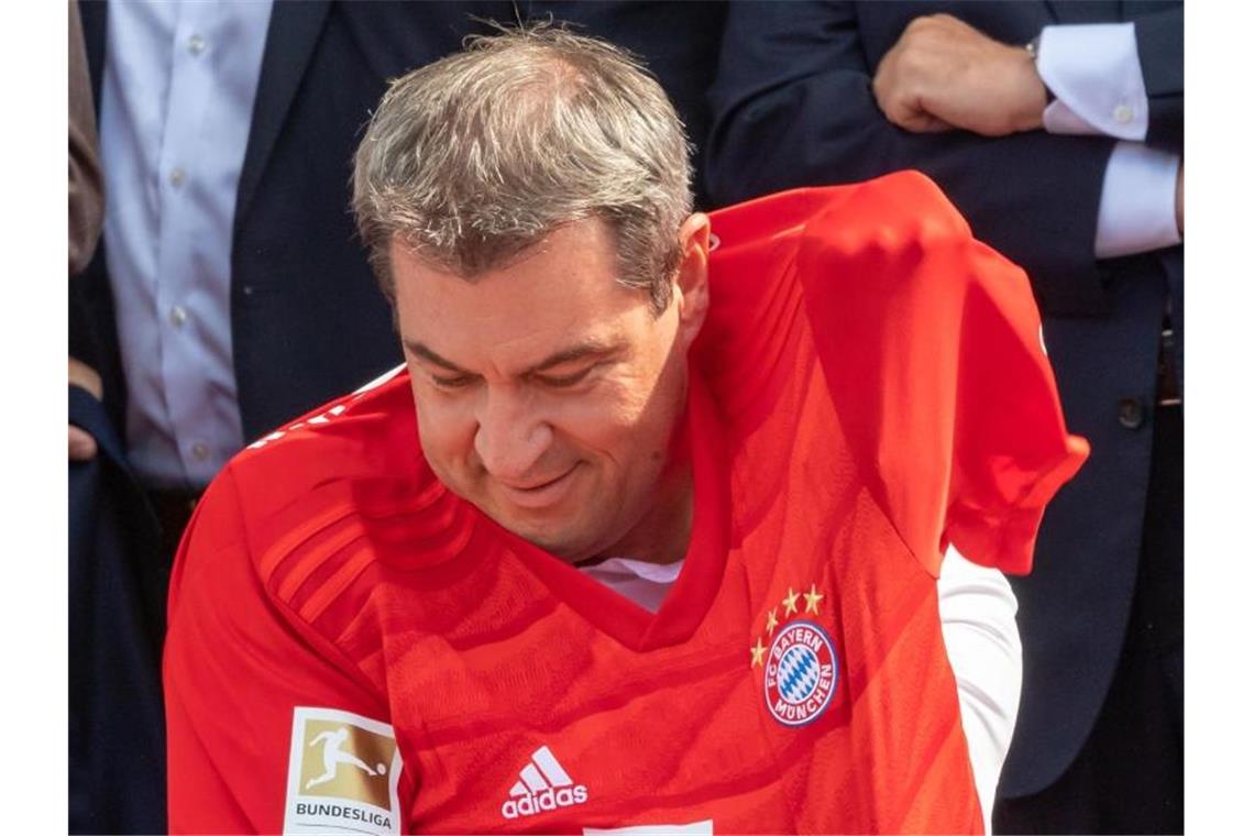 Bayerns Ministerpräsident Markus Söder zwängt sich in ein Trikot des FC Bayern München, das ihm zuvor Uli Hoeneß überreicht hat. Foto: Peter Kneffel
